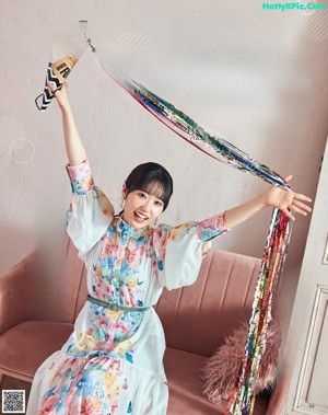 A woman sitting on a couch holding a bunch of balloons.