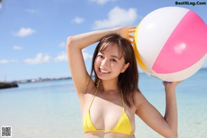 A woman in a yellow bikini standing on a beach.