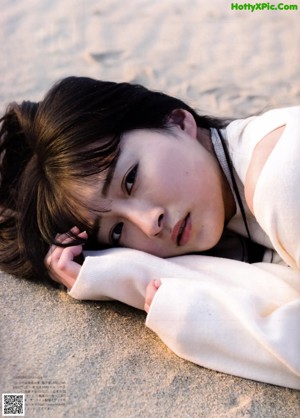A woman in a white dress laying on the sand.