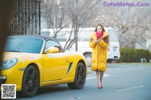 A woman in a yellow coat is posing for a picture.