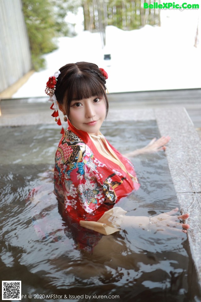 A woman in a red kimono is sitting in the water.
