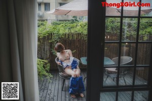 A naked woman standing on a balcony next to a chair.