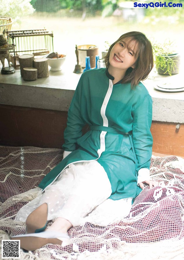 A woman in a green shirt and white skirt sitting on a blanket.